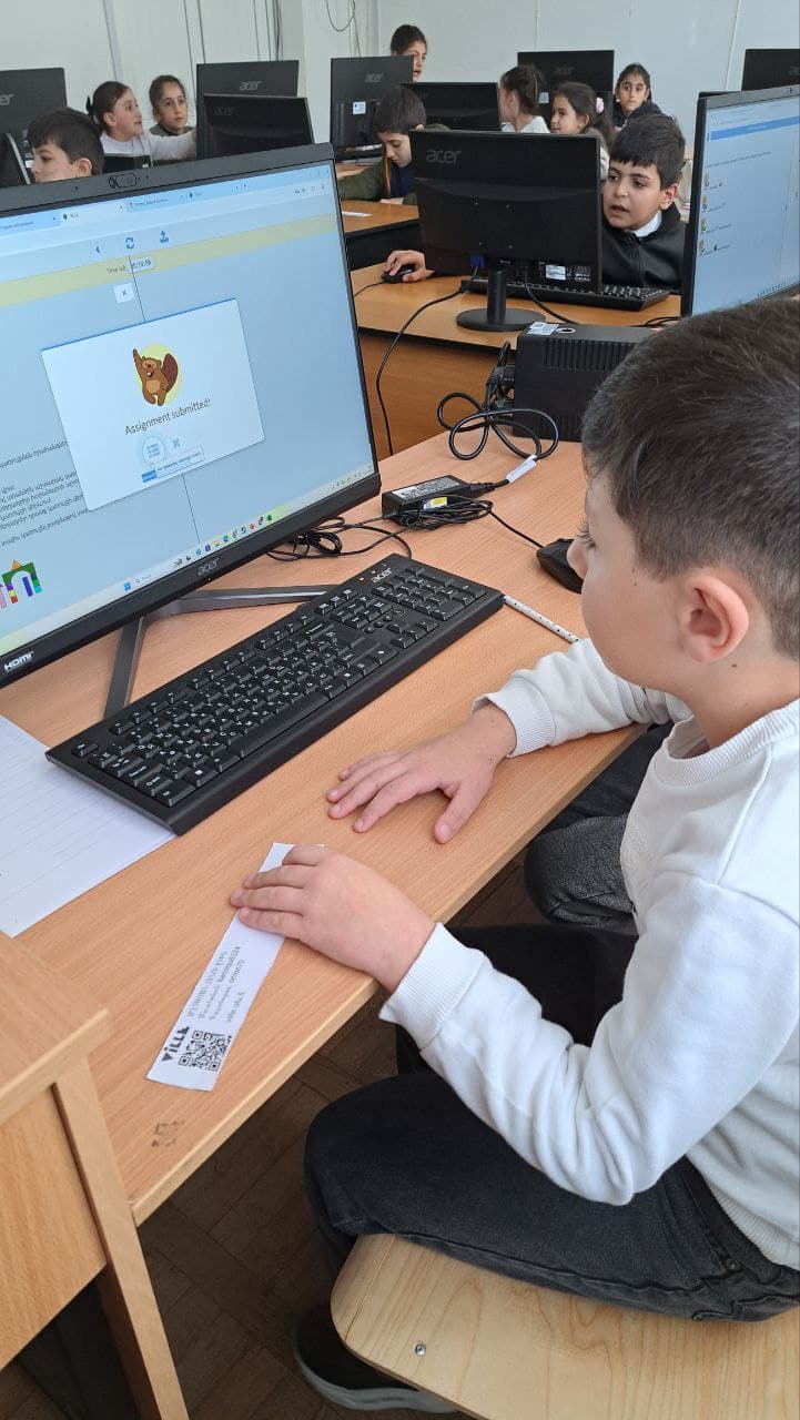 A student sits back from the keyboard, hands flat on the desk, looking at the finished task on screen.