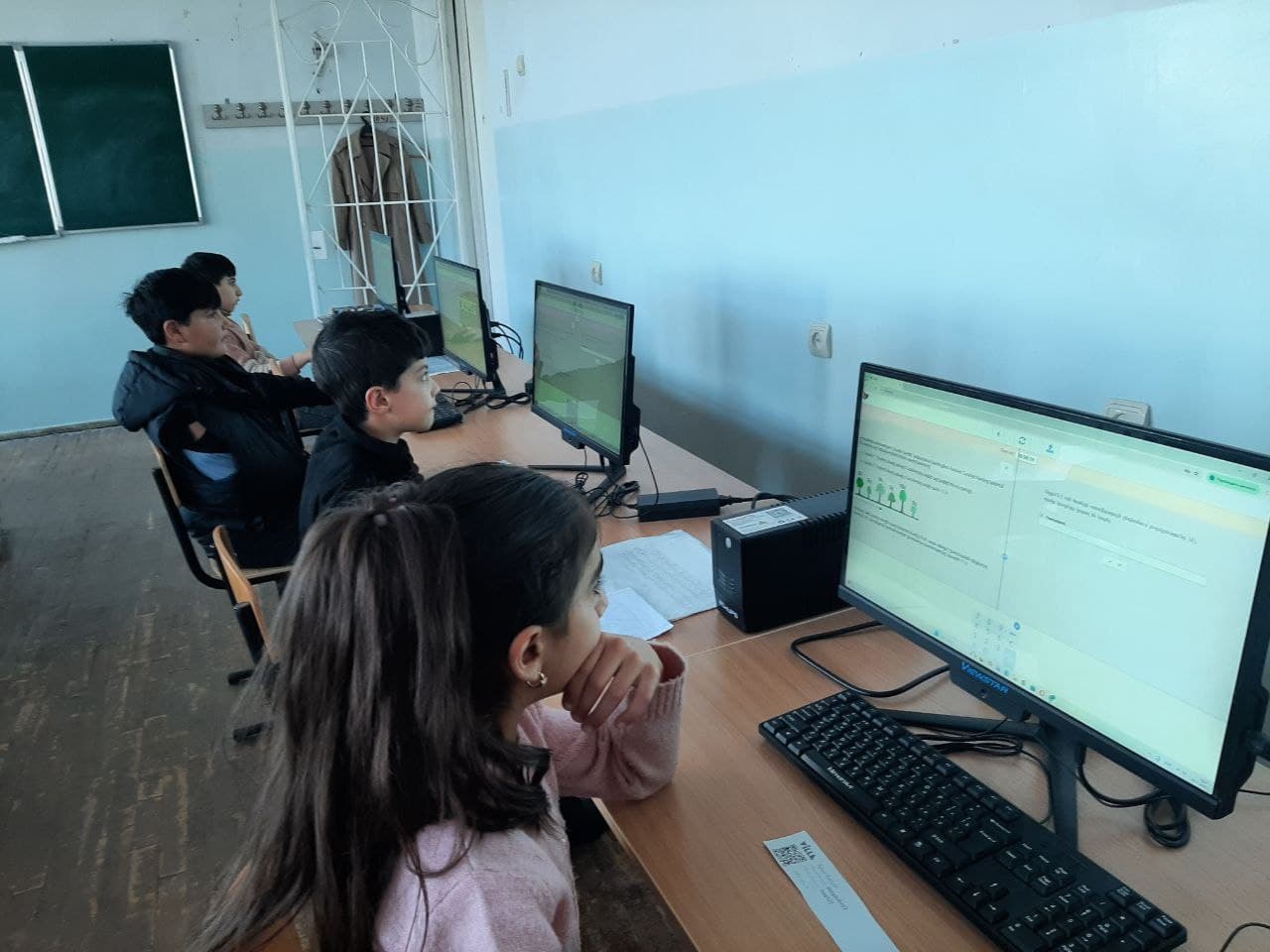 A student sits with her hand at her chin, working through a Bebras task on the monitor in front of her.
