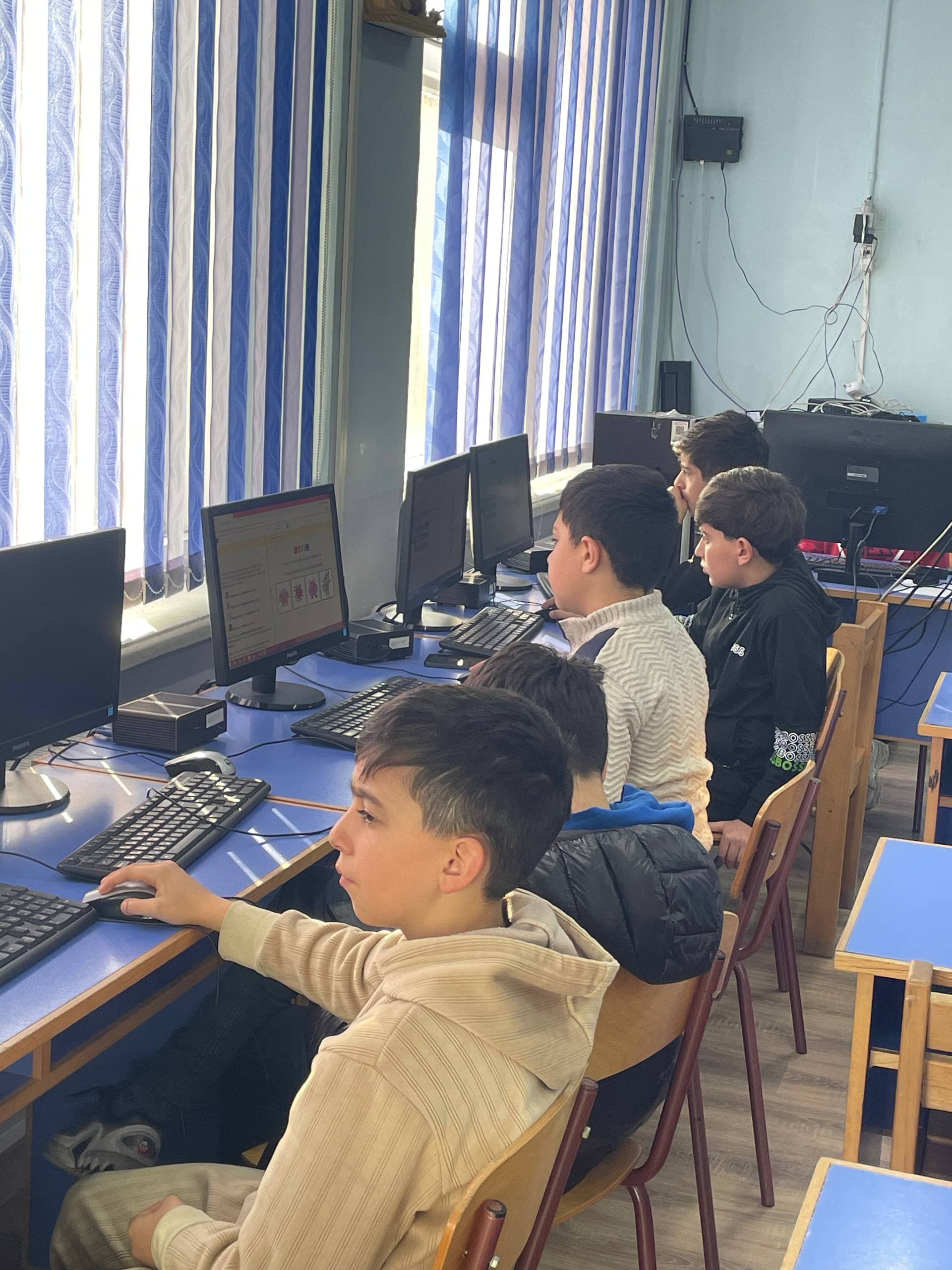 Four students in a row at their monitors, the nearest concentrating on a Bebras task.