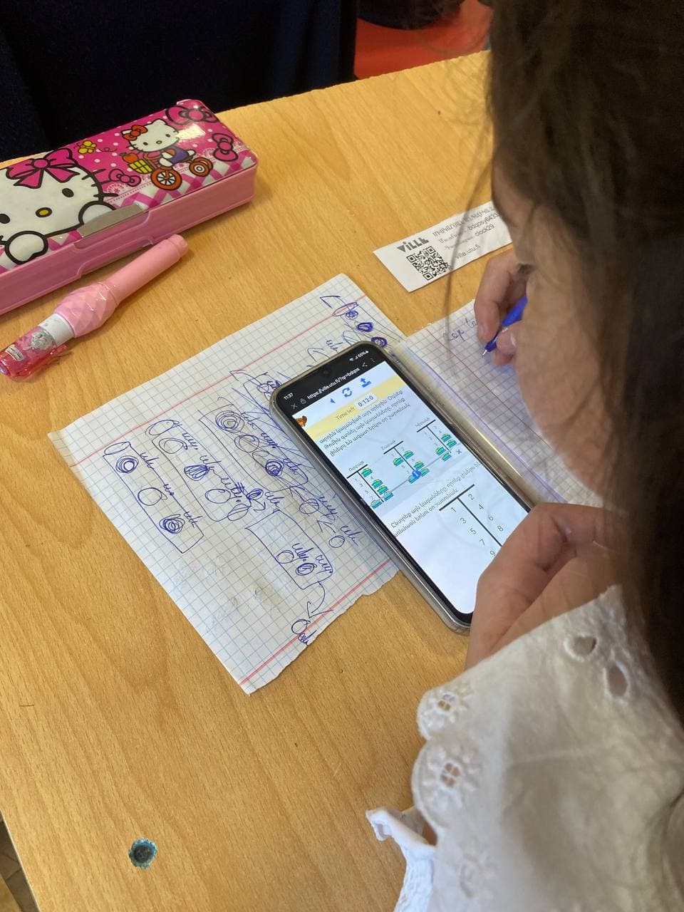 A girl solves a Bebras task on her phone, her own working-out on a sheet of graph paper beside it.