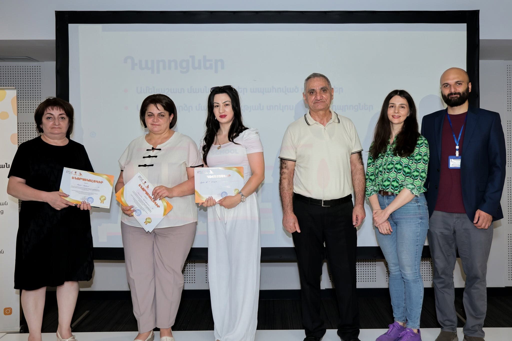 Группа учителей на сцене церемонии награждения, у каждого в руках сертификат.